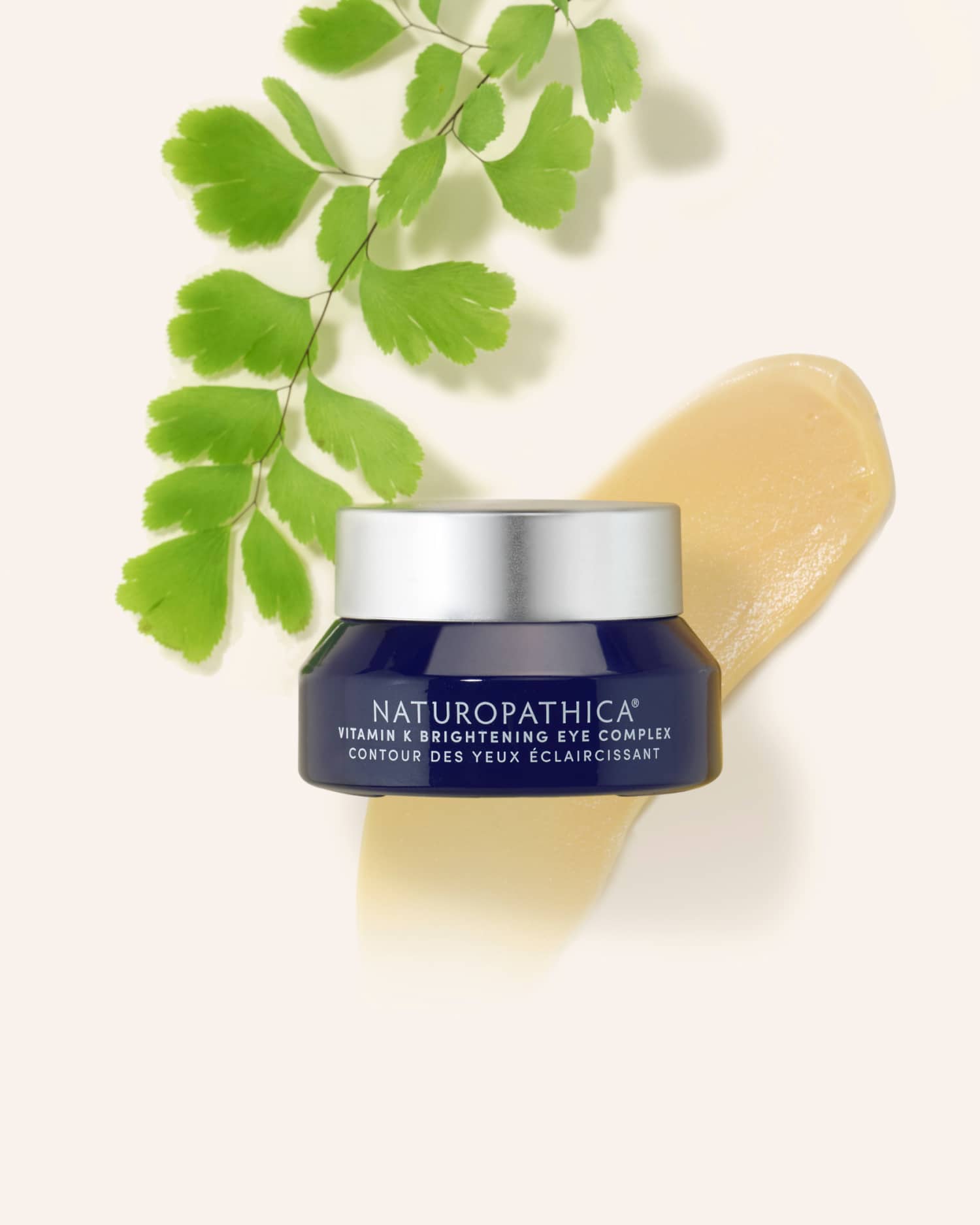 Jar of Naturopathica Vitamin K Brightening Eye Complex with cooling metal applicator and floral accents, styled for de-puffing and brightening eye care


